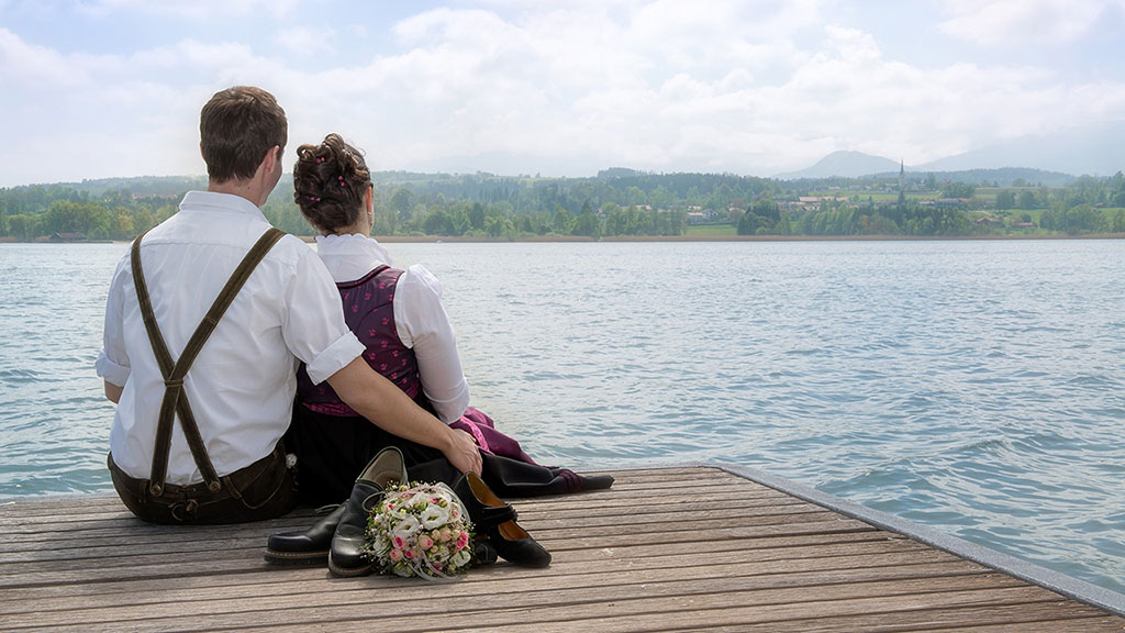 Hochzeitsfotos vom Ehepaar auf einem Steg im Simssee und die Berge im Chiemgau im Hintergrund